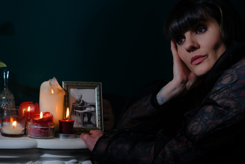 Carol Hodge in a promotional shot for the Manoeuvres single, showing her looking thoughtful by a table on which there are candles and a single framed photo